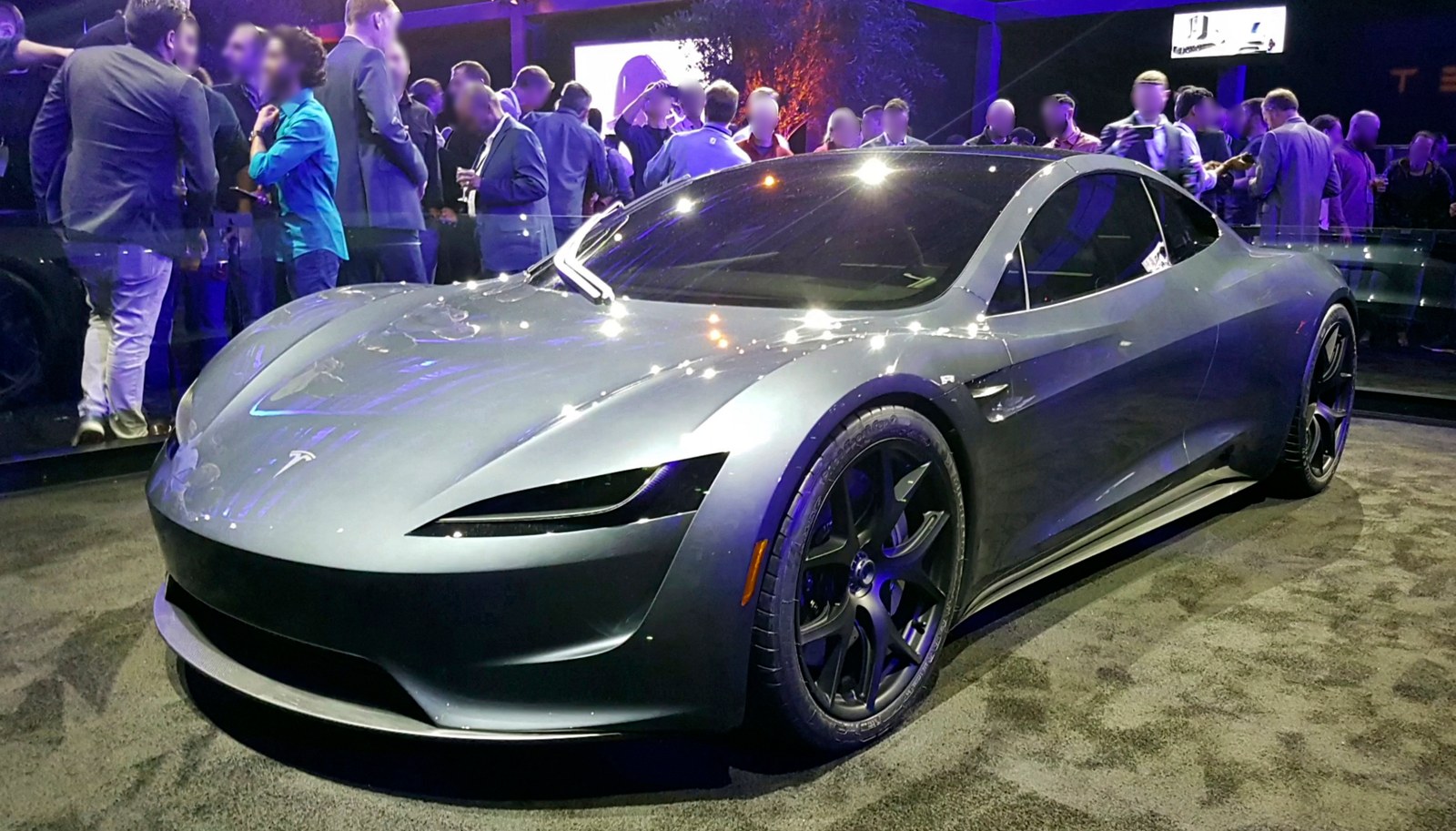 The silver-gray second-generation Tesla Roadster prototype shown from a front three-quarter angle on the event floor at its November 2017 unveiling, a blurred audience with blue and purple stage lights behind it